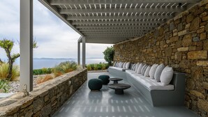 An outdoor seating area with a stone wall and a view of the sea. - VILLA FAROS NEAR PORT, MYKONOS BY MYKONOS AGENDA (Mykonos)