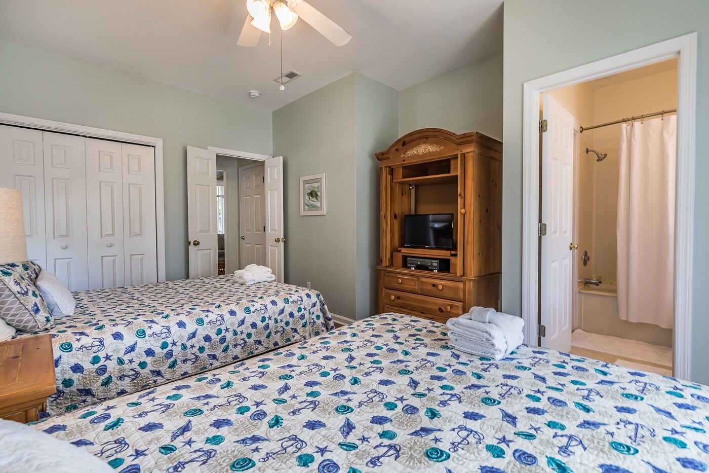 A bedroom with two beds, a wooden TV stand, and a bathroom door.