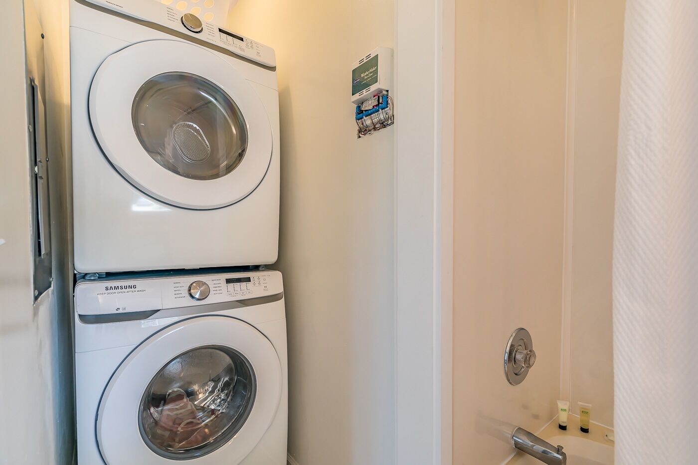 A laundry room with two stacked washing machines and a door with a towel dispenser.