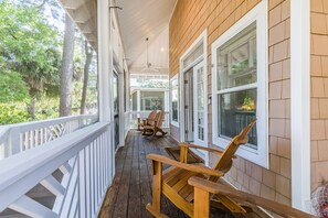 A covered porch with wooden chairs, white railings, and large windows. - “Playin’ Through” - Pet Friendly, Golf Cart included, Club Cards available - 22 Davis Love (Fripp Island)