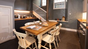 Une cuisine avec une table en bois, des chaises blanches, un escalier et une fenêtre.