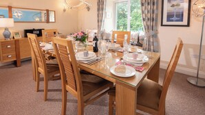 A dining area with a glass table set for four, surrounded by wooden chairs. - Overbeck, Ambleside - Two Bedroom Cottage, Sleeps 4 (Ambleside)
