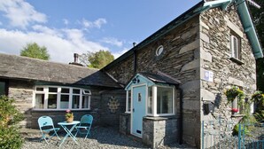 A stone building with a small attached structure, a gravel patio with two chairs, and a window with a flower box. - Overbeck, Ambleside - Two Bedroom Cottage, Sleeps 4 (Ambleside)