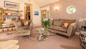 A cozy living room with a sofa, armchairs, a glass coffee table, and a bookshelf filled with books. - Overbeck, Ambleside - Two Bedroom Cottage, Sleeps 4 (Ambleside)