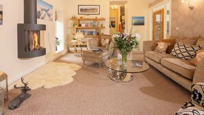 A cozy living room with a fireplace, a sofa, a coffee table, and a bookshelf. - Overbeck, Ambleside - Two Bedroom Cottage, Sleeps 4 (Ambleside)