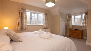 Une chambre avec un grand lit, deux fenêtres avec des rideaux, une commode en bois et un radiateur.