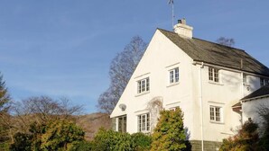 Une maison blanche à deux étages, dotée d’un toit à forte pente, de nombreuses fenêtres et d’une cheminée.