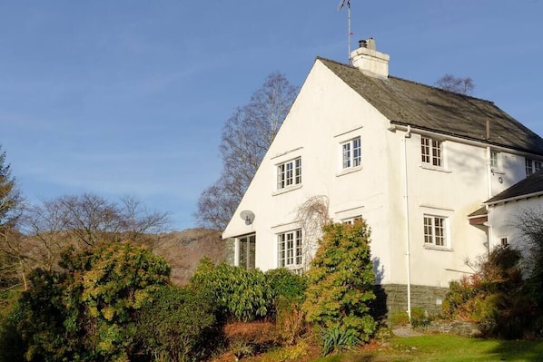 A white two-story house with a steeply pitched roof, multiple windows, and a chimney.