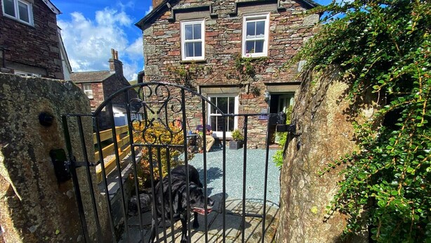 A stone building with a gated entrance, a paved driveway, and a large tree with dense foliage. - Juniper Grasmere - Juniper Cottage, Grasmere (Grasmere)
