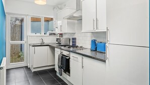 Cocina compacta con alacenas blancas, estufa a gas, microondas y cafetera.