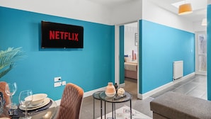 Una sala de estar moderna con una pared verde azulado, un televisor de pantalla plana mostrando 