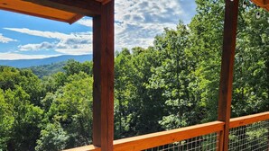 A wooden deck with a metal railing overlooking a forested area with mountains in the distance. - New 5BR Cabin w/ Pool, Hot Tub • Near Smokies (Sevierville)