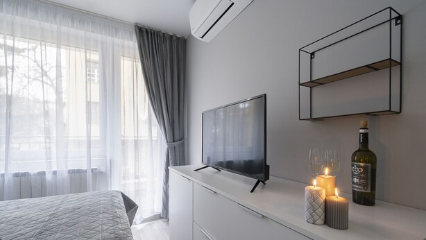 Un dormitorio moderno con cama, televisor de pantalla plana, una botella de vino y velas sobre una mesita de noche.