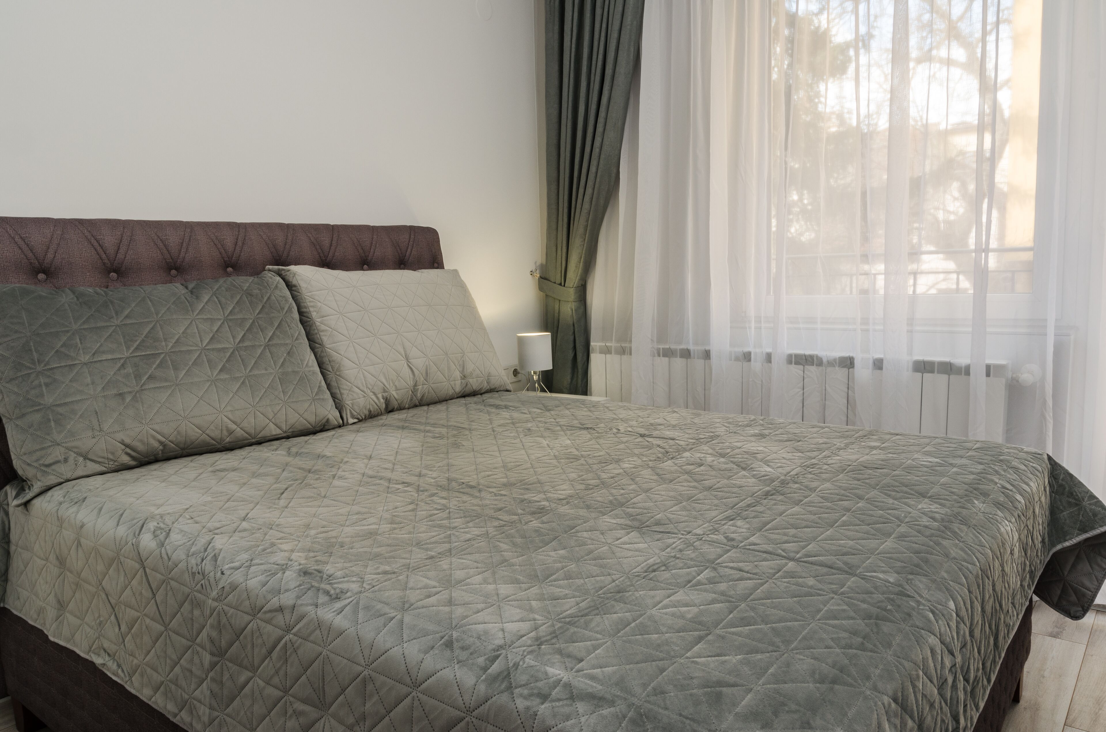 A bed with a quilted headboard and a bedside table with a lamp.