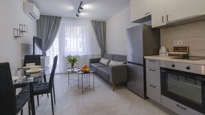 Una cocina moderna con horno integrado, una zona de comedor con mesa de vidrio y un sofá gris.