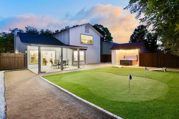 A house with a covered patio, a lawn with flags, and a wooden fence.