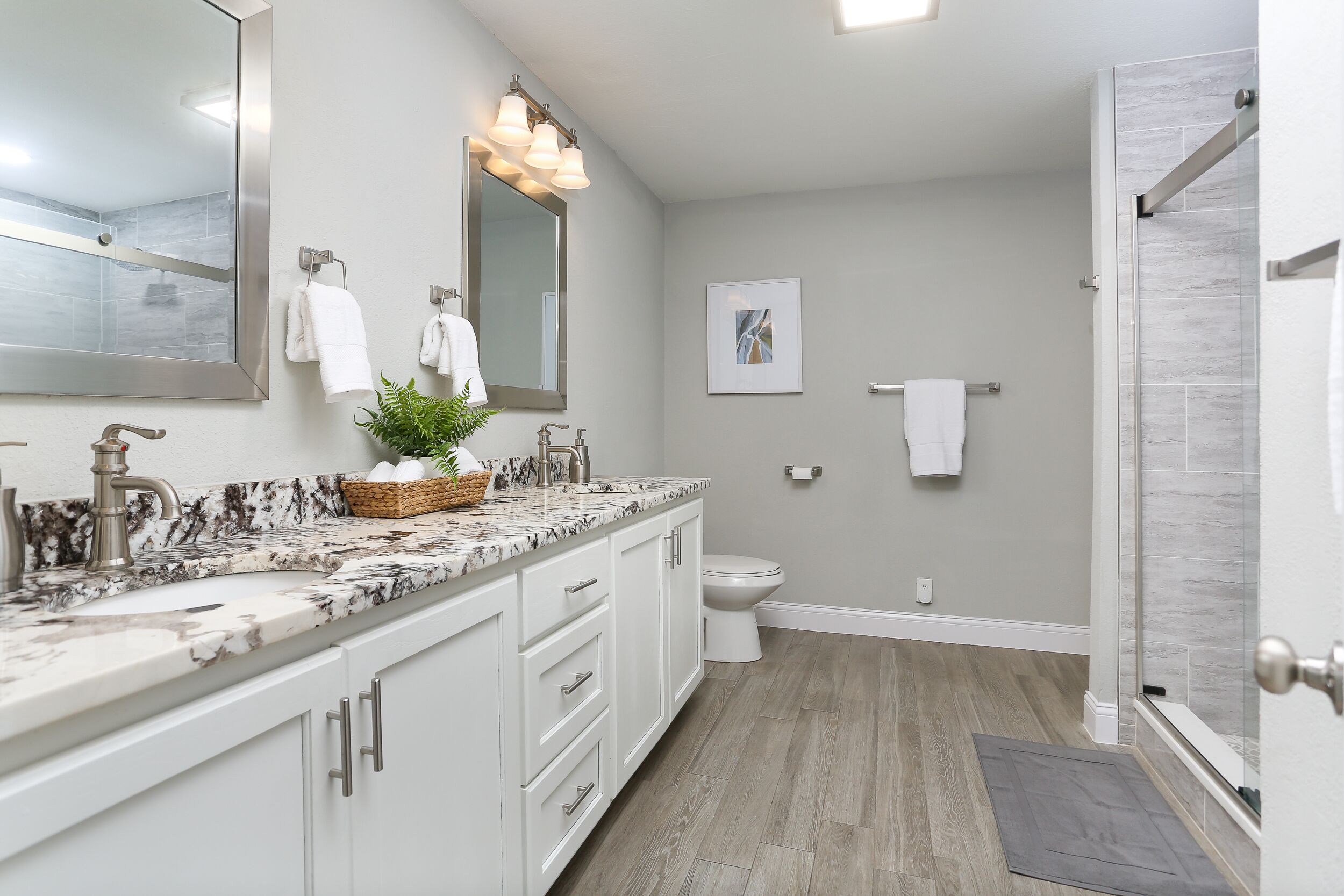 A modern bathroom with a marble countertop, a large mirror, a shower, and a toilet.