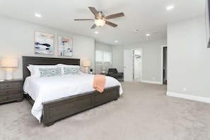 A bedroom with a bed, nightstands, a ceiling fan, and artwork on the walls.