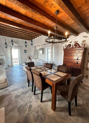 A dining area with a wooden table and chairs, a chandelier, and a stone floor. - Villa Oikia Suites  Mykonos  (Mykonos)