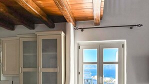 Eine kompakte Küche mit weißen Schränken, ein Essbereich mit Tisch und Stühlen sowie ein Fenster mit Meerblick.