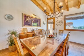Un comedor con mesa de madera, sillas, una lámpara de araña y vistas al exterior.