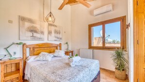A bedroom with a wooden headboard, a bed with patterned bedding, a hanging light fixture, a window with a view, and a radiator. - Mallorquin Finca piscina CA'S SOLLERICH en Mallorca (Inca)