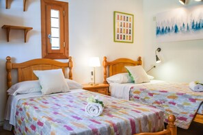 Habitación de hotel con dos camas de madera, una ventana, un estante en la pared y un cuadro.