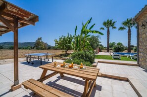 Una terrazza all'aperto con un tavolo da ping pong, un tavolo di legno con bevande e una zona piscina.