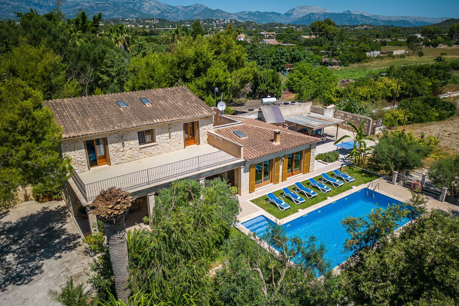 Una casa a due piani con piscina, immersa nel verde con montagne sullo sfondo.