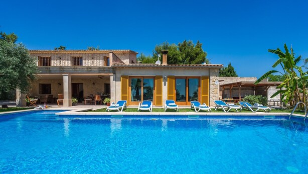 A poolside view of a resort with a clear blue pool, sun loungers, and a building with large windows and shutters. - Mallorquin Finca piscina CA'S SOLLERICH en Mallorca (Inca)
