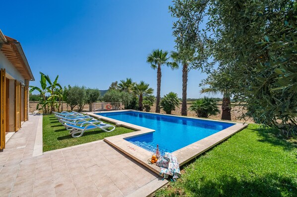Una piscina con sillones de descanso, un suelo de baldosas y un cielo azul despejado.