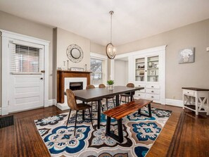 Uma sala de jantar com mesa de madeira, cadeiras e um banco. Há um tapete estampado no chão.