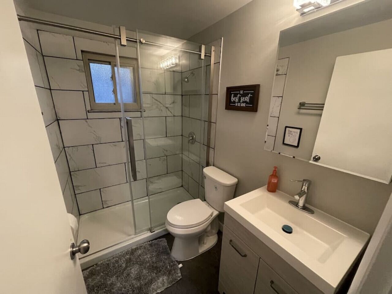 A modern bathroom with a glass shower enclosure, a toilet, a sink, and a mirror.