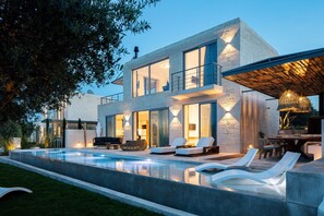 Una casa moderna de dos pisos con piscina, mobiliario exterior y un patio cubierto.