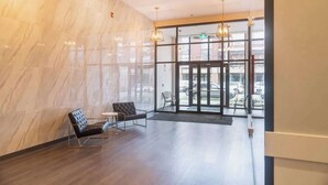 Een moderne lobby met marmeren wanden, een zwarte leren bank en een glazen deur naar buiten.