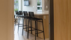 Een moderne keuken met een houten aanrecht, drie zwarte barkrukken en hanglampen.