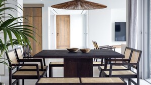 Un espace repas moderne avec une table en bois foncé, six chaises et un grand luminaire suspendu en forme de parasol tressé.