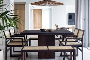 Een moderne eetruimte met een donker houten tafel, zes stoelen en een grote geweven lamp.