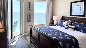 Een slaapkamer met een groot bed, een plafondventilator, een nachtkastje met een lamp en uitzicht op de oceaan door een schuifdeur.