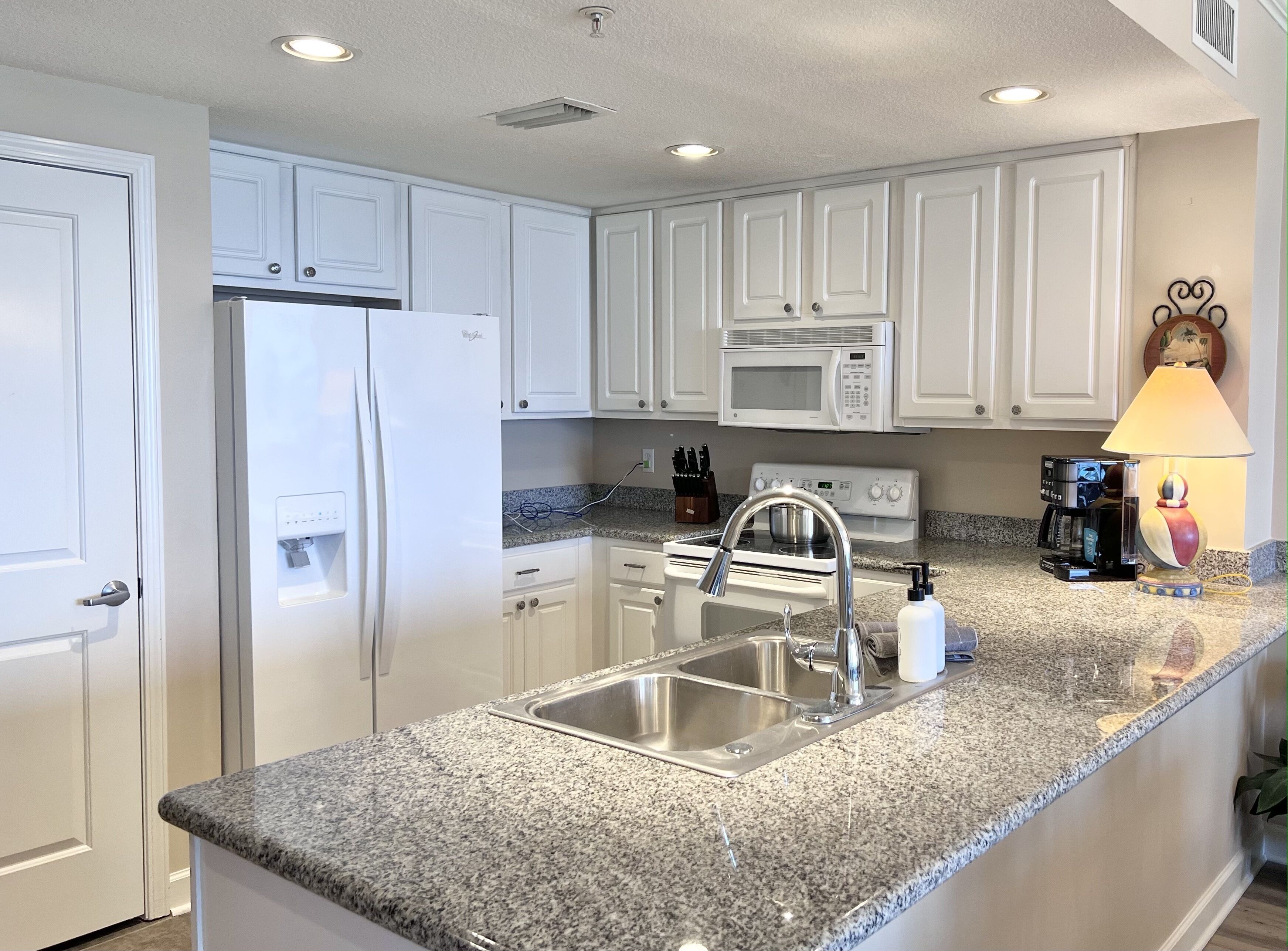 A modern kitchen with white cabinets, a stainless steel sink, a built-in microwave, and a granite countertop.