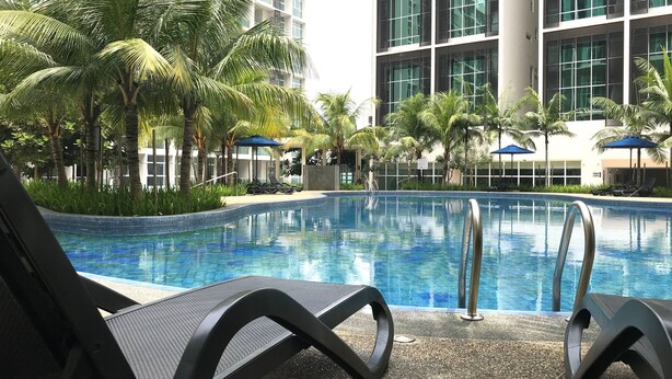 Una piscina con sillas de descanso y palmeras, rodeada de edificios modernos.