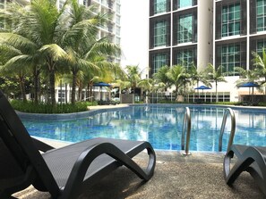 Une piscine entourée de chaises longues et de palmiers, le tout bordé d’immeubles modernes.
