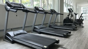Varias cintas de correr en un gimnasio con amplios ventanales y suelo de madera.