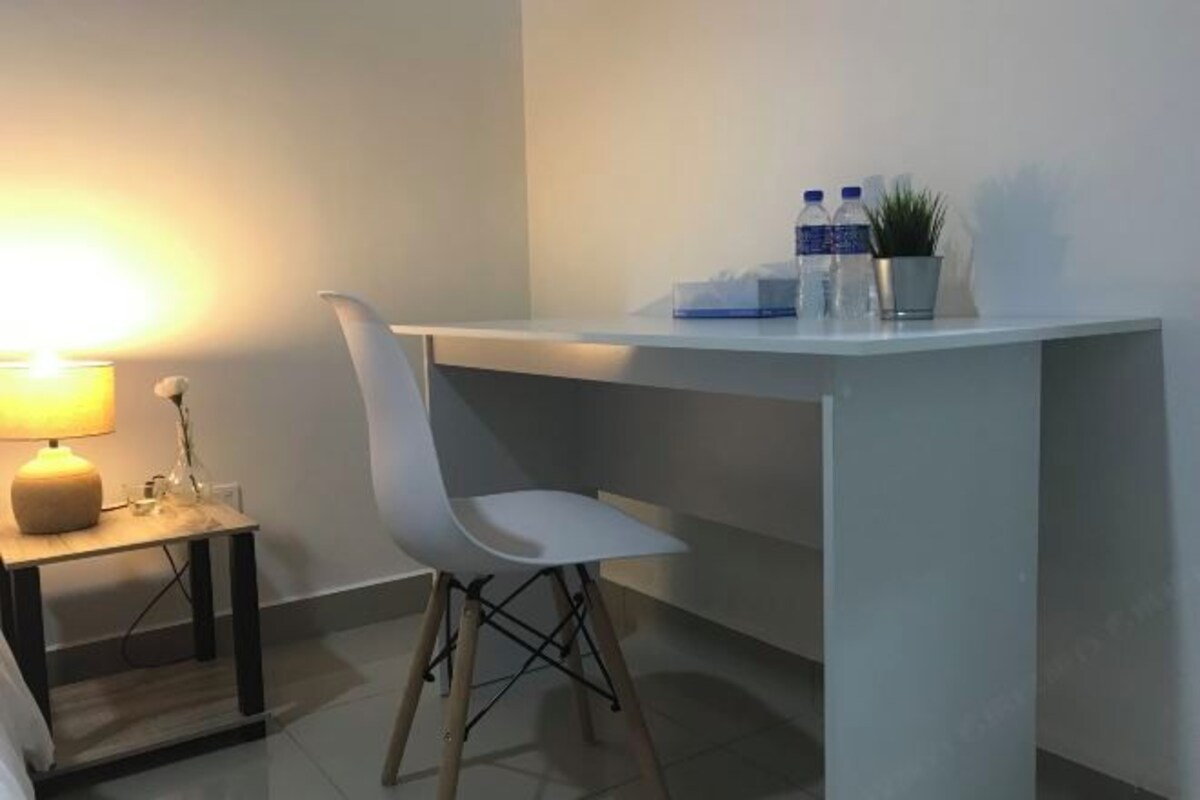 Une chambre moderne avec un bureau blanc, une chaise, une lampe et une petite plante en pot.