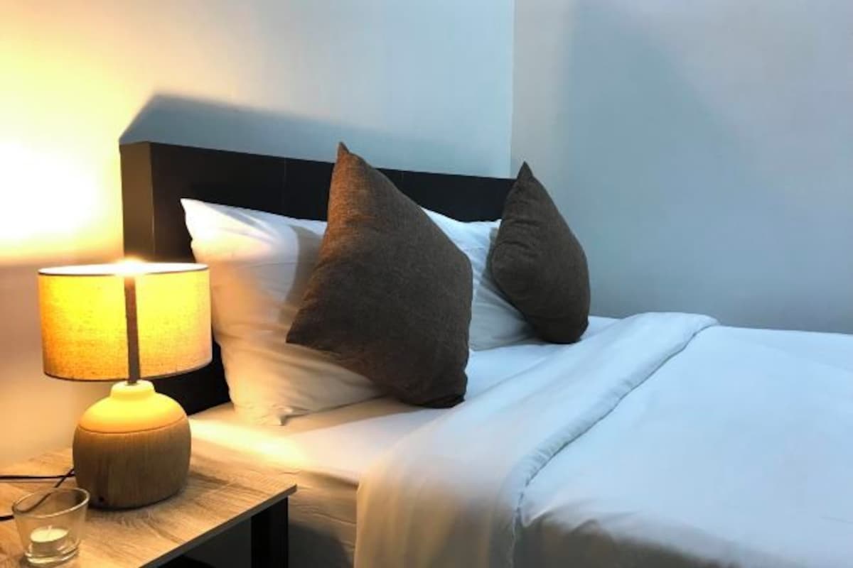 Un lit bien fait, avec une tête de lit, une lampe de chevet et un verre d’eau sur une table de chevet.