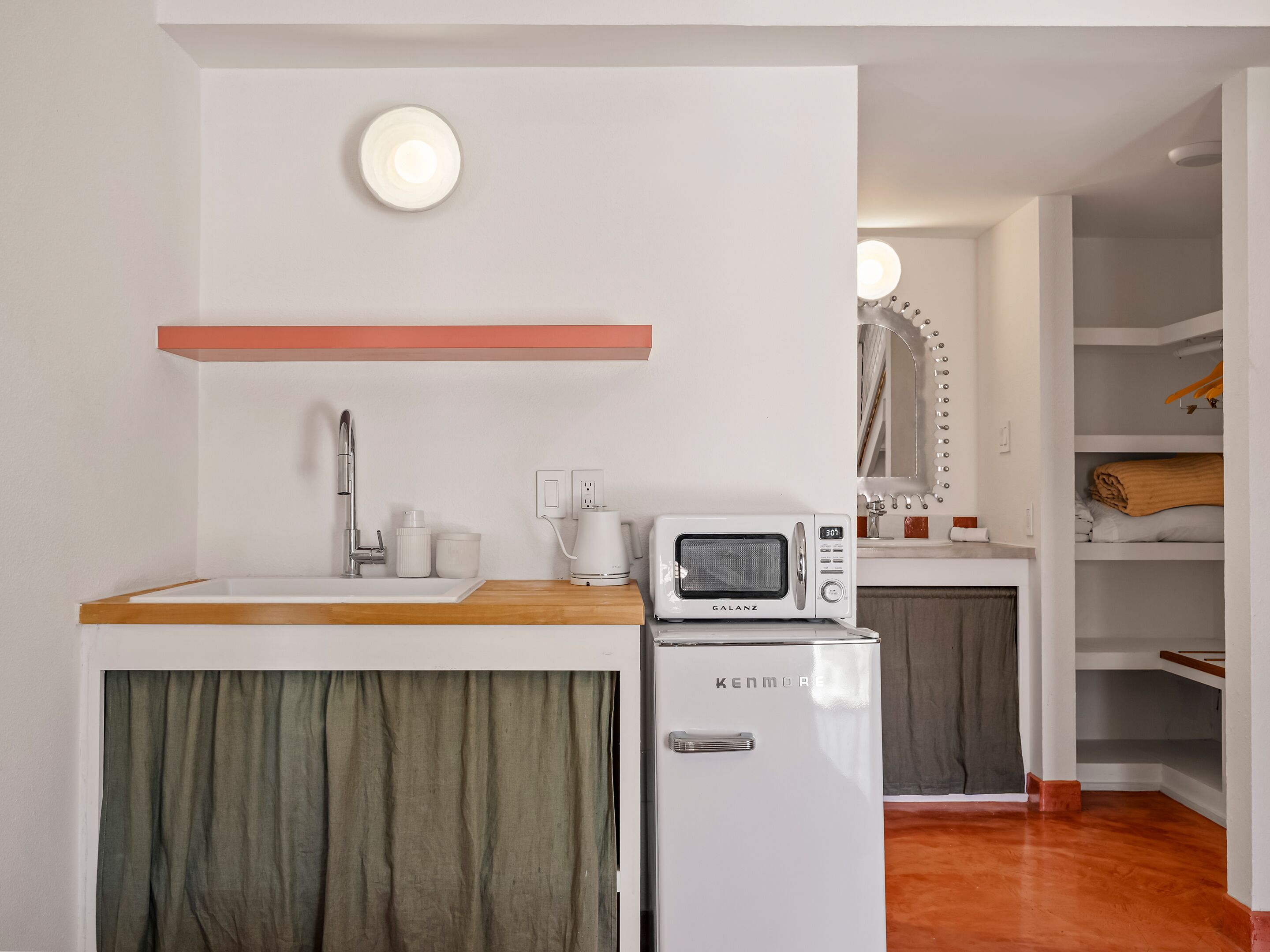 Cocina compacta con lavamanos, grifo, microondas y un refrigerador pequeño.