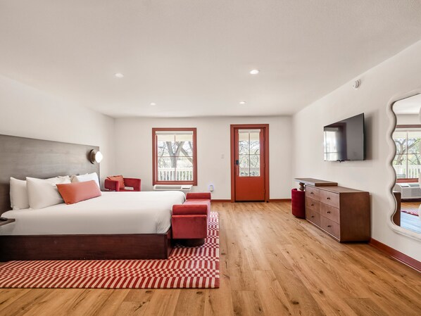 A bedroom with a bed, a dresser, a TV, and a door. - Hacienda del Rio (New Braunfels)