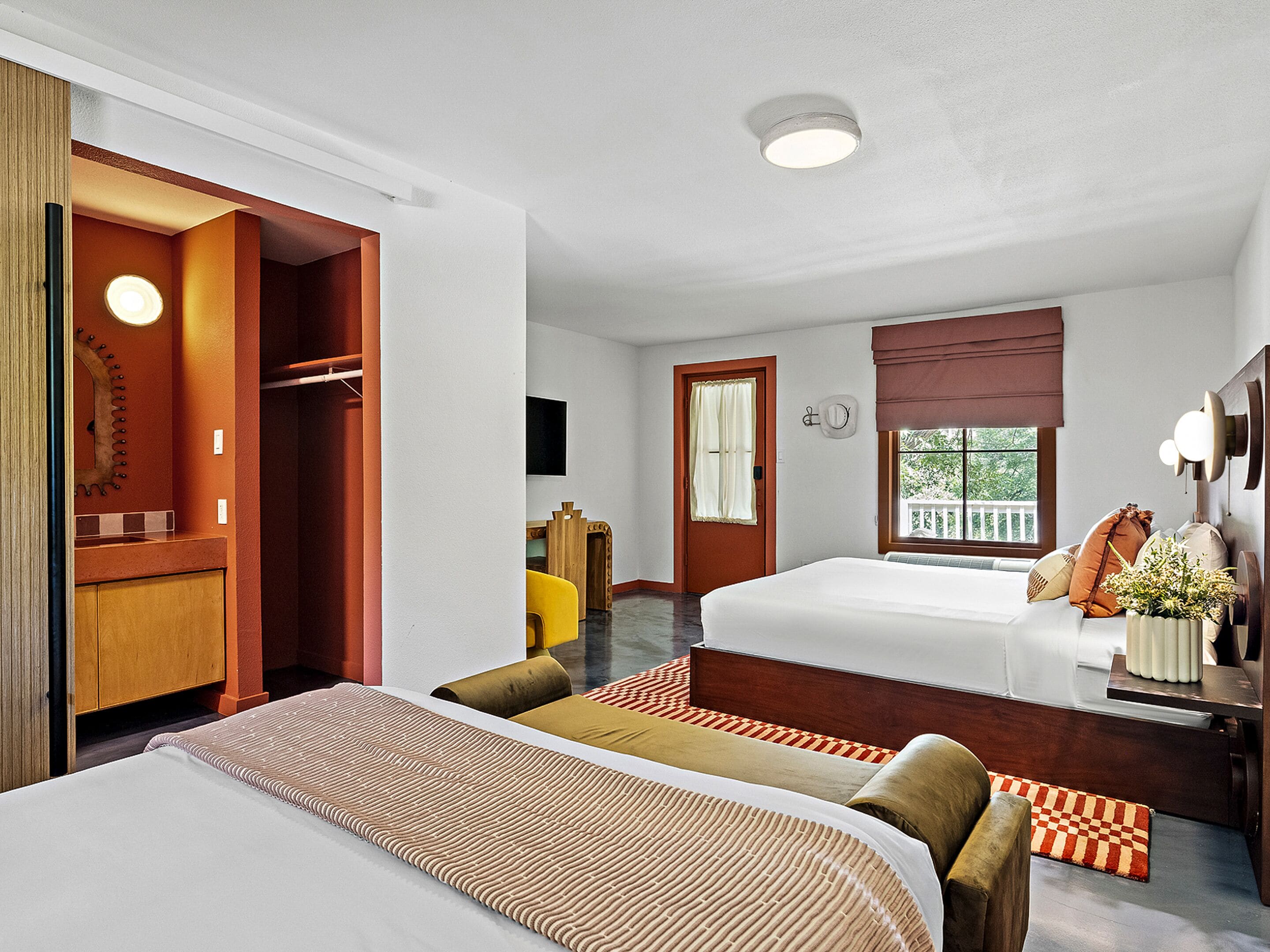 A hotel room with two beds, a wardrobe, a desk, and a window with a view.