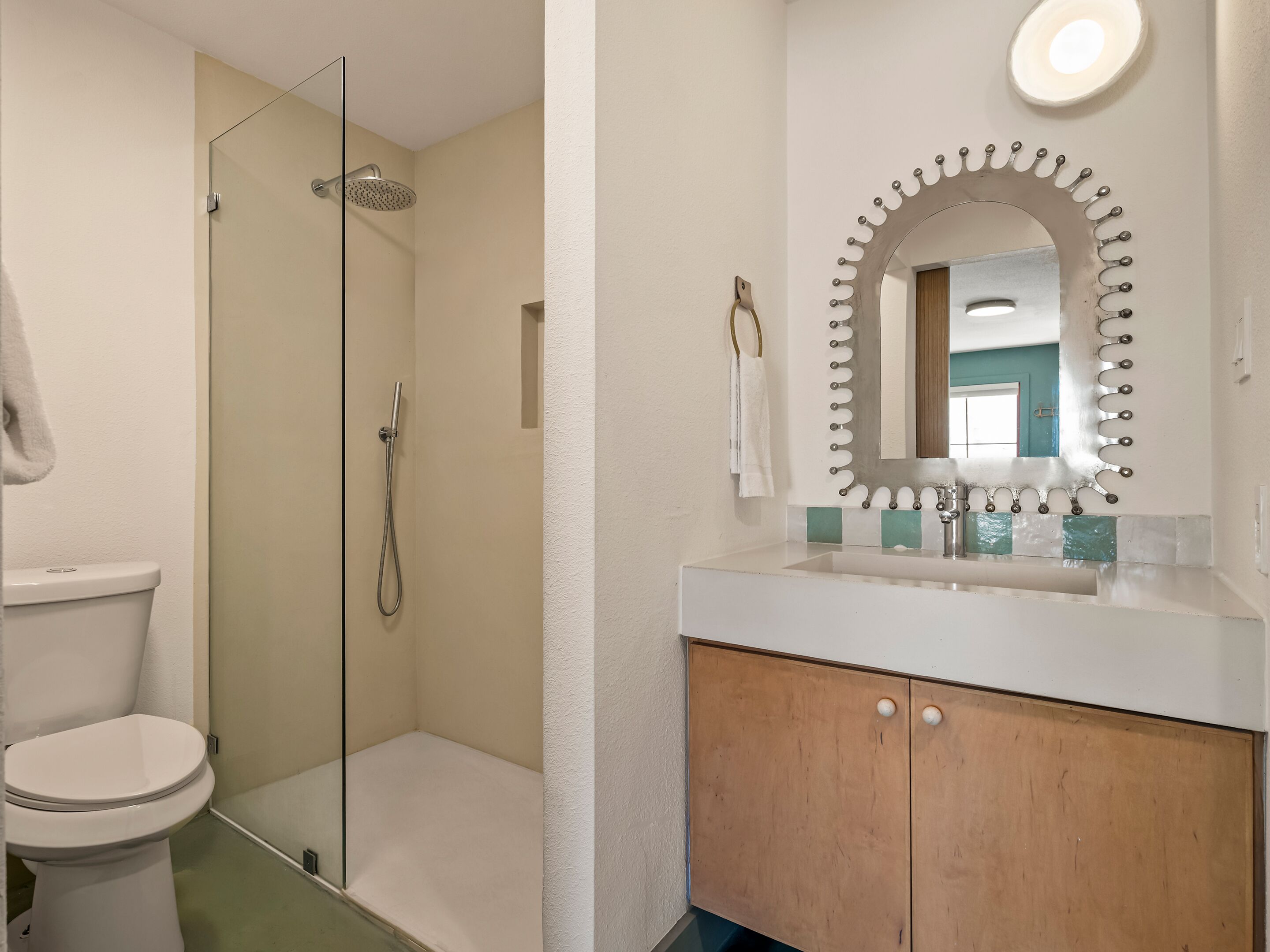 Un baño con cabina de ducha de vidrio, inodoro blanco, tocador de madera con espejo y salpicadero de azulejos.