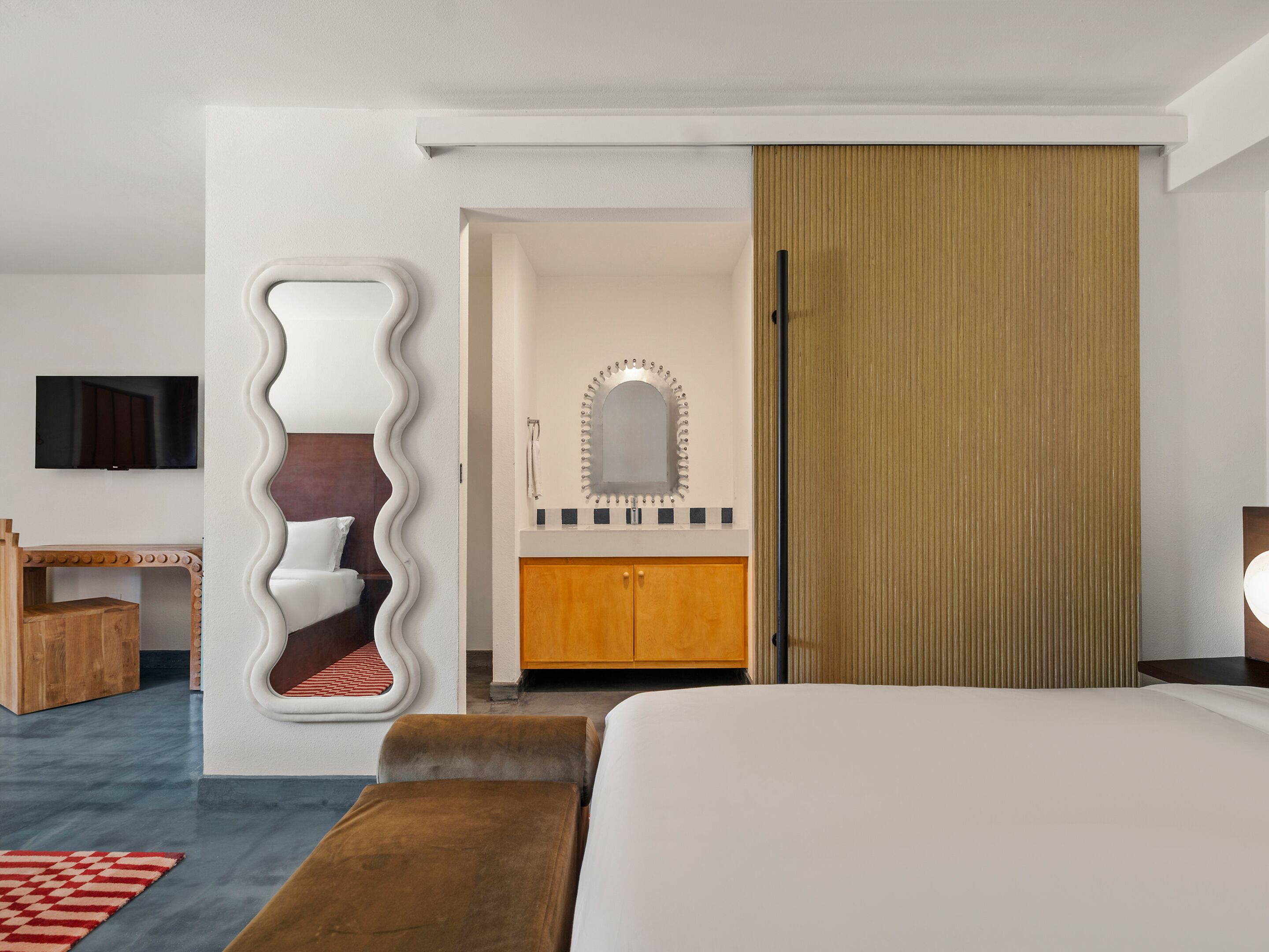A modern hotel room with a large bed, a wooden cabinet, a mirror, and a television.